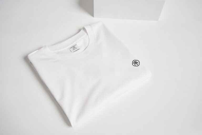A minimalist folded white t-shirt on a white background showcasing simple and clean fashion style.