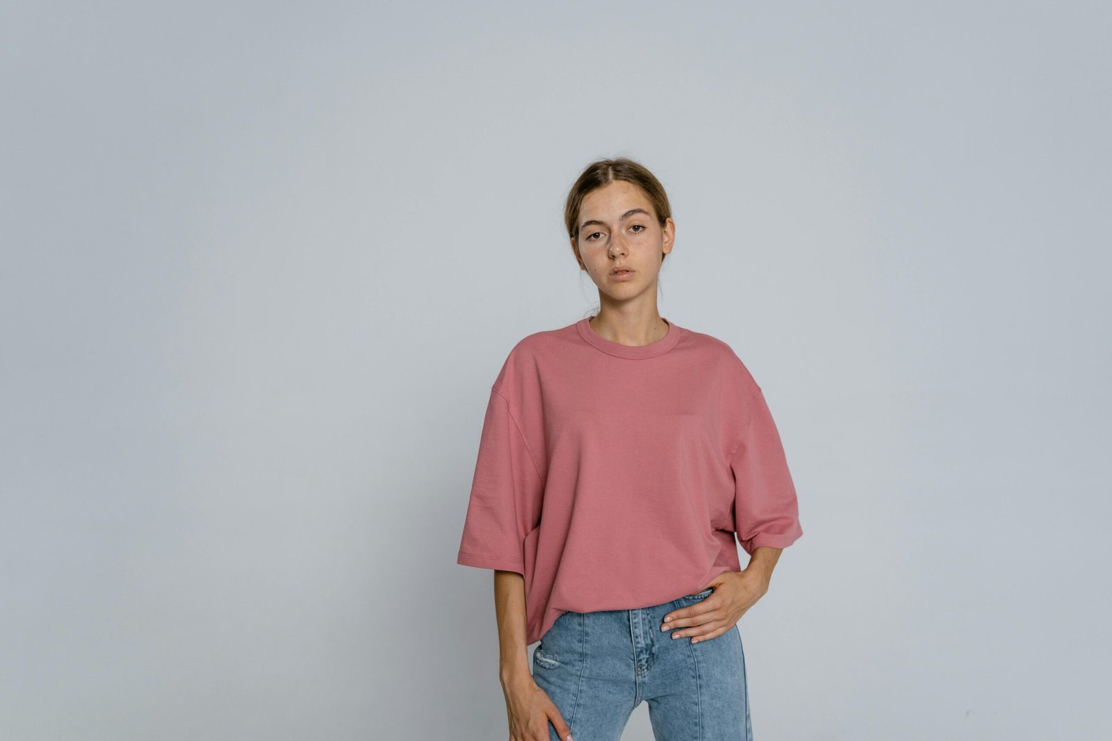 Portrait of a young woman standing in a relaxed pose wearing a pink t-shirt and jeans.